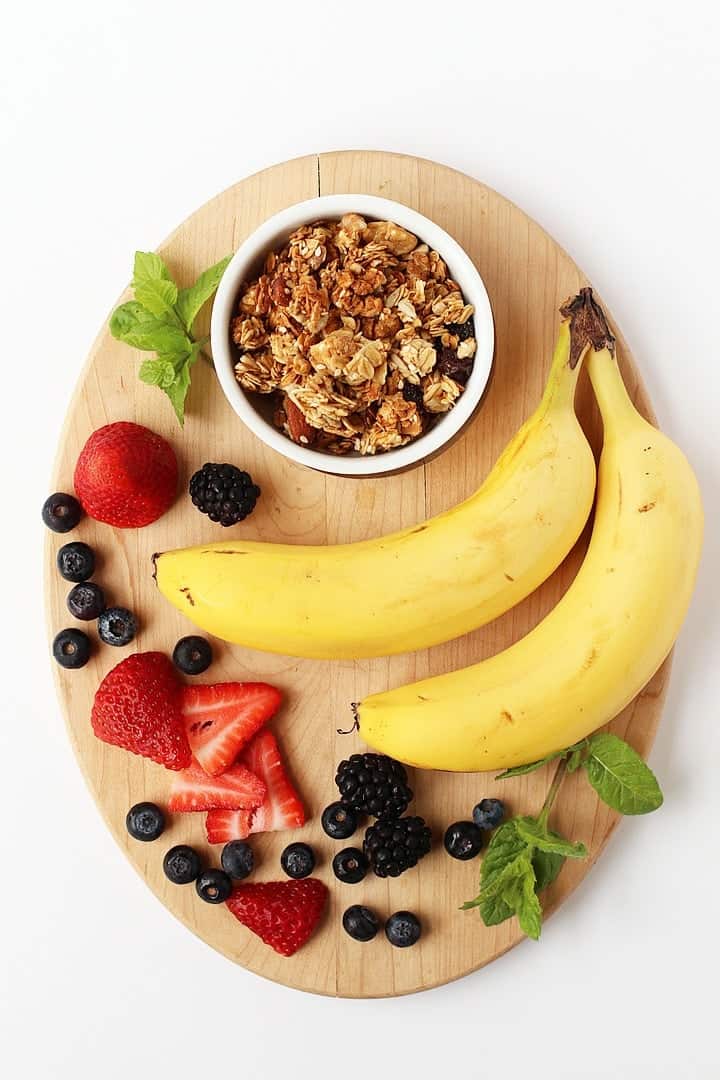 Bananas, berries, and granola on a wooden platter