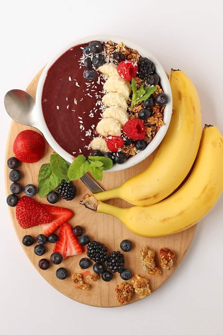 Smoothie bowl on a wooden platter with berries and bananas