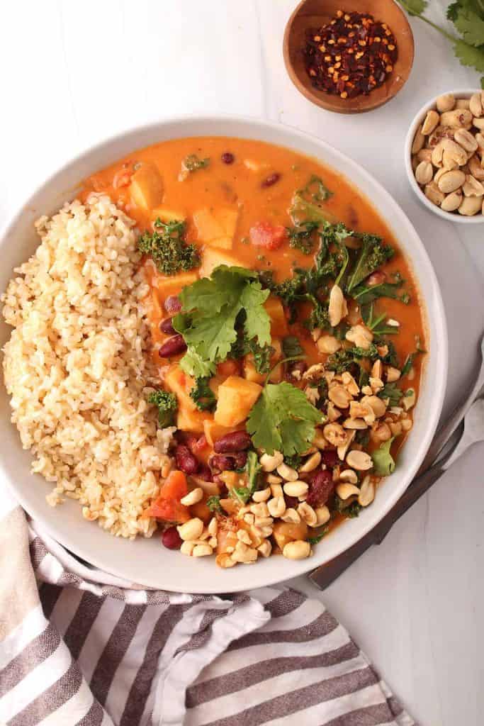 overhead shot of a white bowl of rice and vegan peanut stew garnished with peanuts and fresh cilantro
