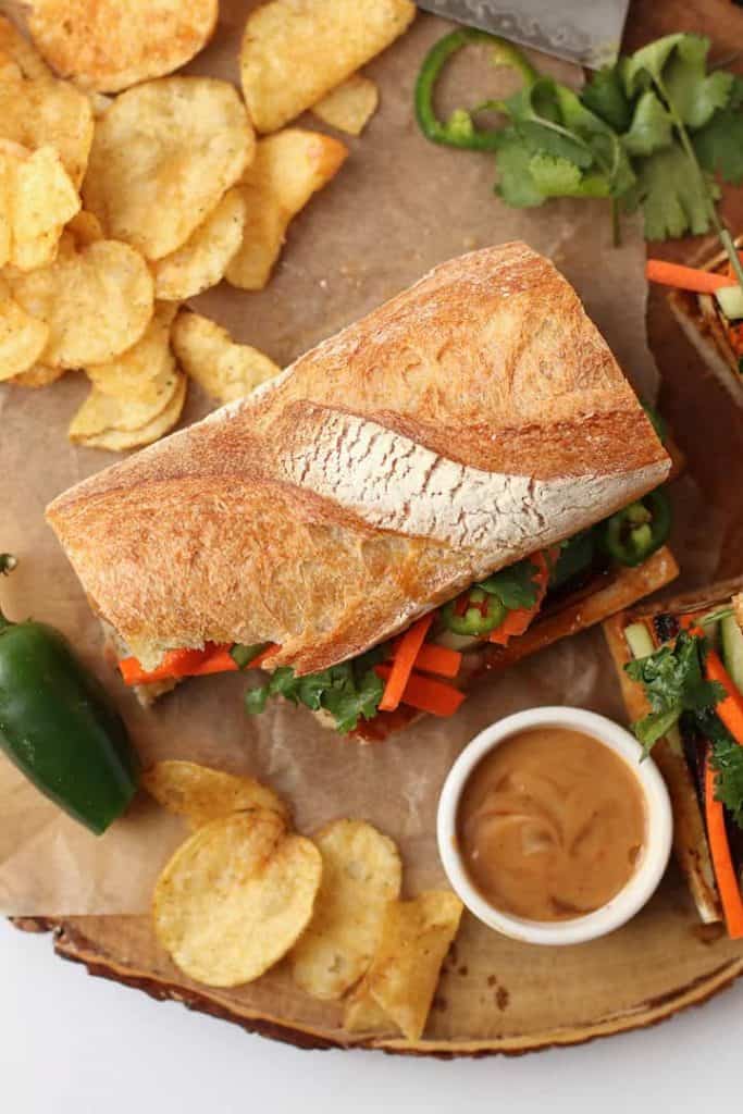 Finished Bahn mi sandwich on a wooden board with chips