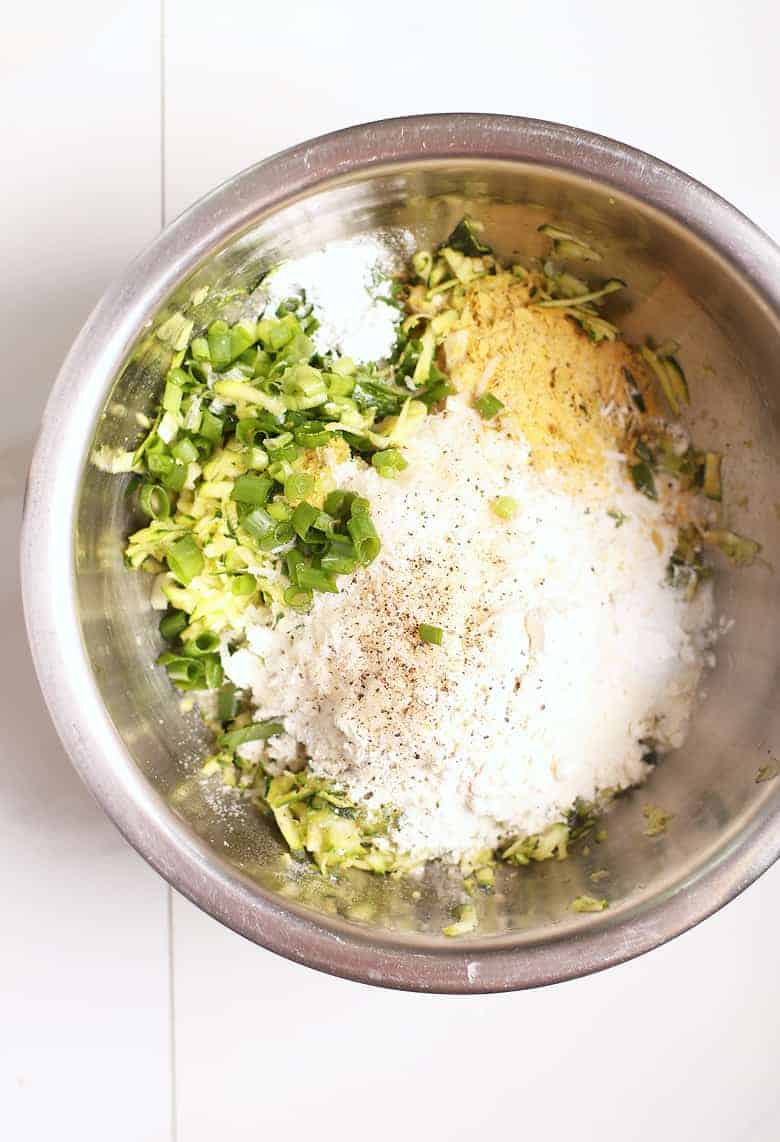 Shredded zucchini, flour, onions, and nutritional yeast in a metal bowl