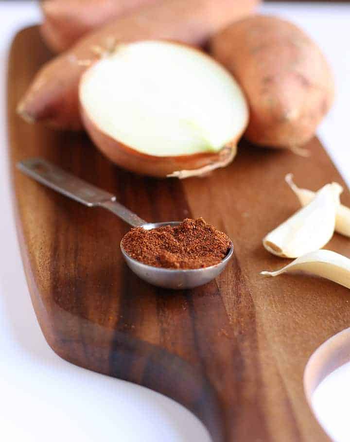 Onion, sweet potatoes, and chili powder on wooden board