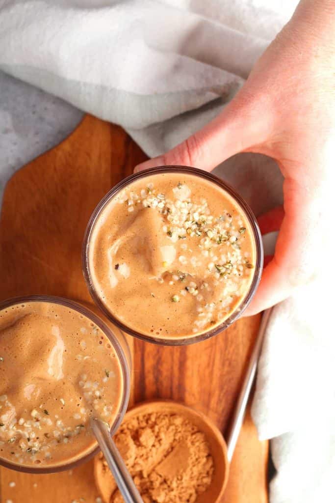overhead shot of a hand reaching for a glass of chocolate breakfast smoothie topped with hemp hearts