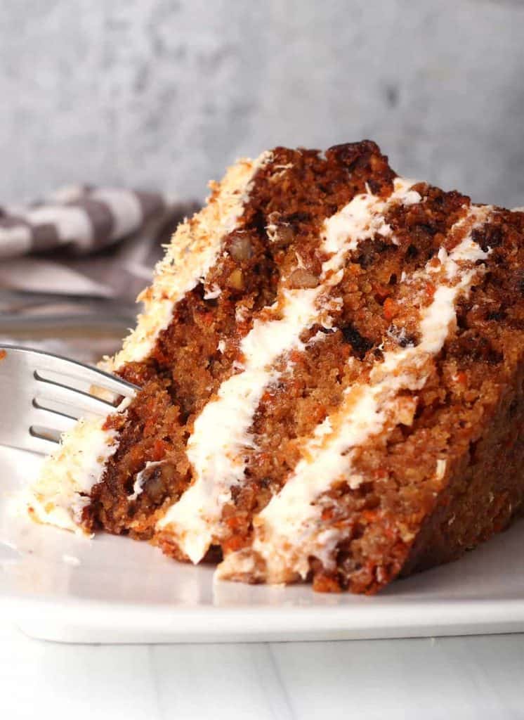 close up of a slice of vegan carrot cake on its side being cut with a silver fork