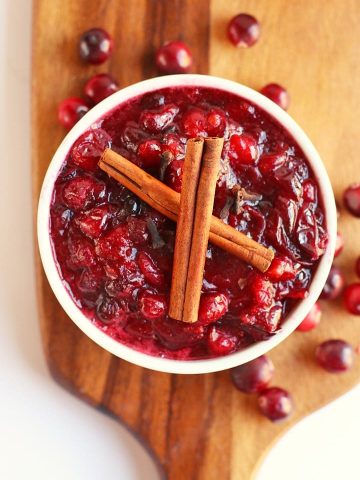 Finished cranberry sauce in a white bowl with two cinnamon sticks
