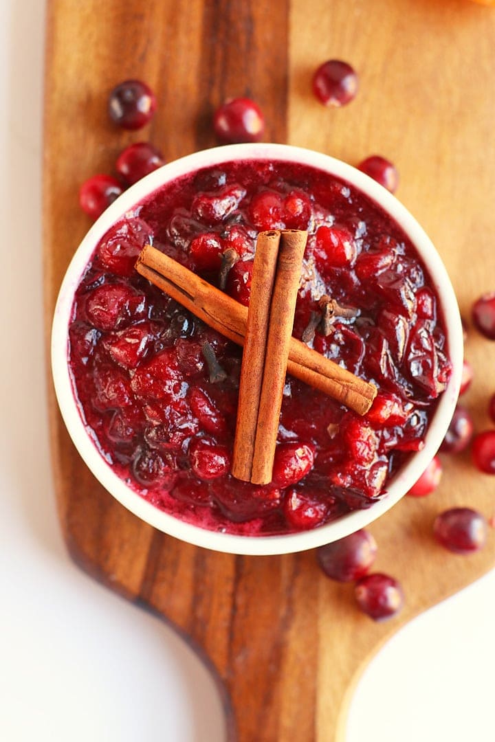 Finished cranberry sauce in a white bowl with two cinnamon sticks