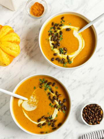 top view of pumpkin curry soup recipe in two bowls with toasted pumpkin seeds and cashew cream