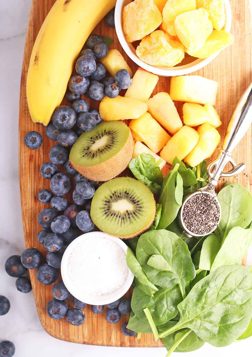 Blueberries, kiwi, banana, and spinach on a cutting board