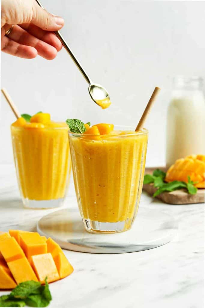 Finished mango smoothies in two glasses with fresh mango and mint. 
