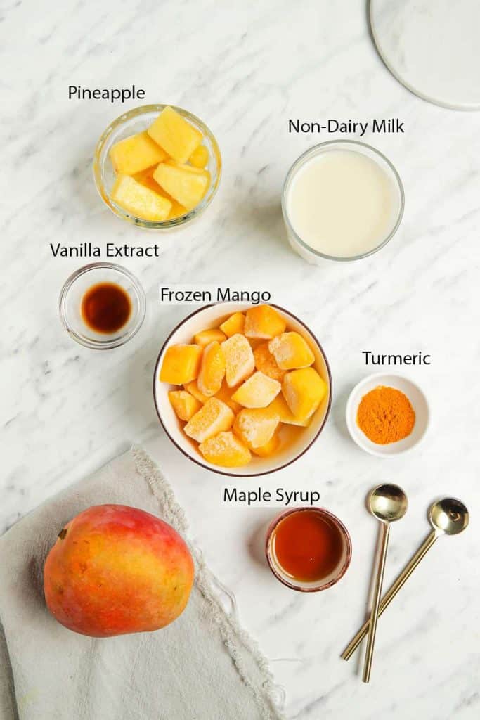 Ingredients for mango smoothie measured out and placed into small bowls on a marble countertop