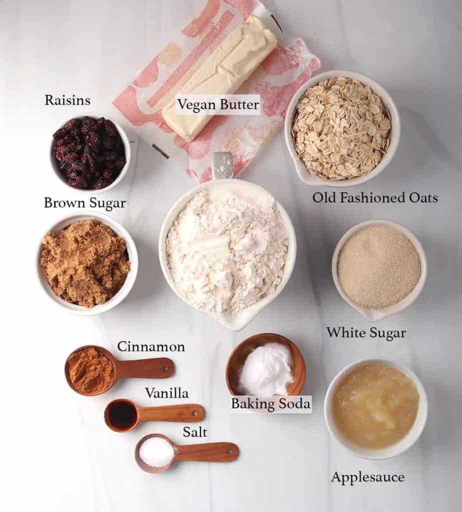 Ingredients for vegan oatmeal raisin cookies measured out and placed on a marble countertop 