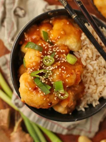 Baked Orange Cauliflower and rice in a black bowl with chopsticks