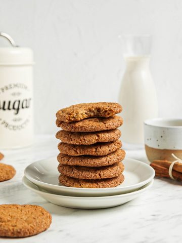 stack of seven pumpkin snickerdoodle cookies on two white plates with cinnamon and milk in background