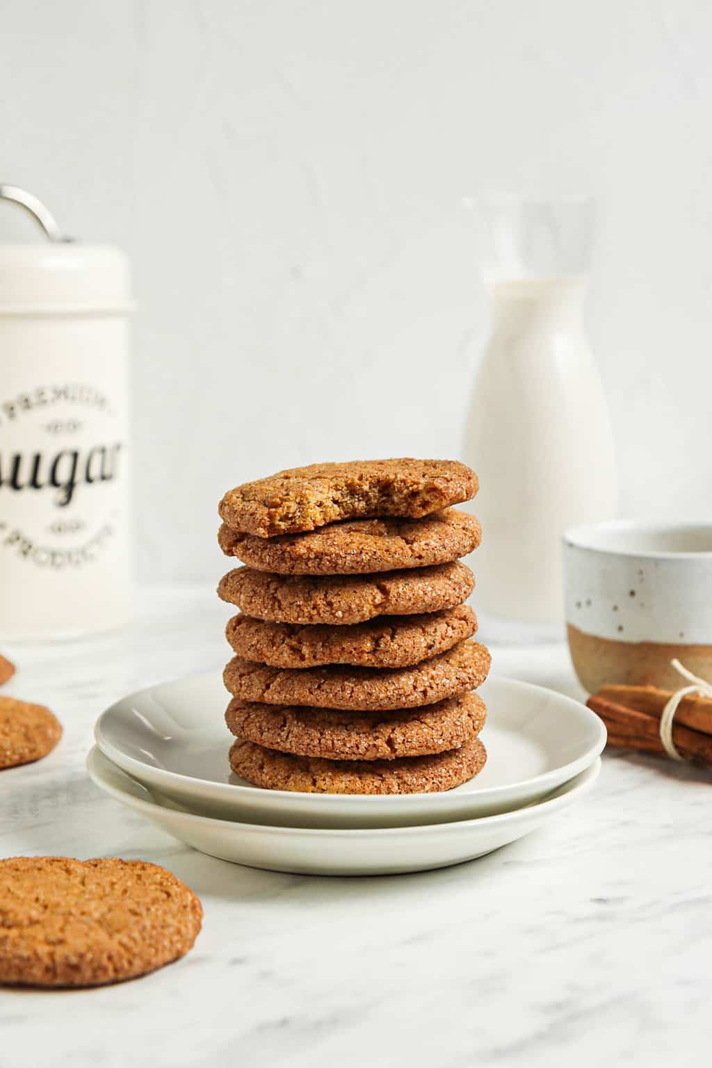 one stack of seven cookies on two white plates with sugar and milk in background 