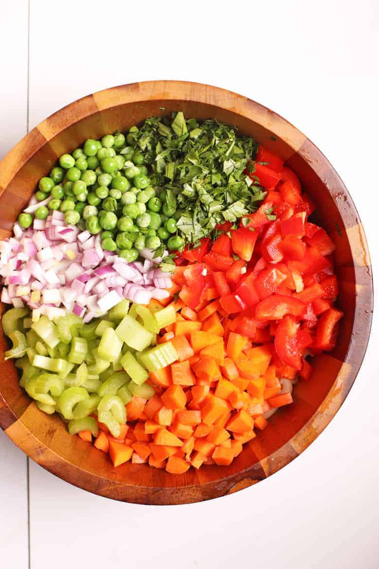 Carrots, celery, onions, peas, and bell pepper in a wooden bowl