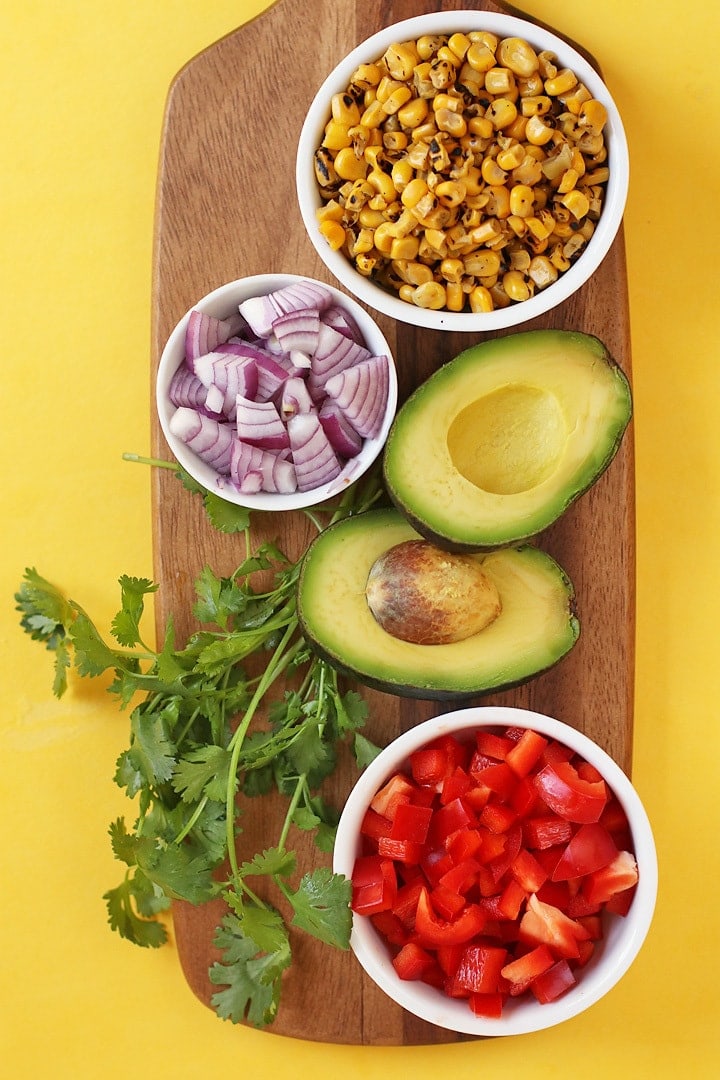 Bell pepper, avocado, corn, and red onion on a wooden board