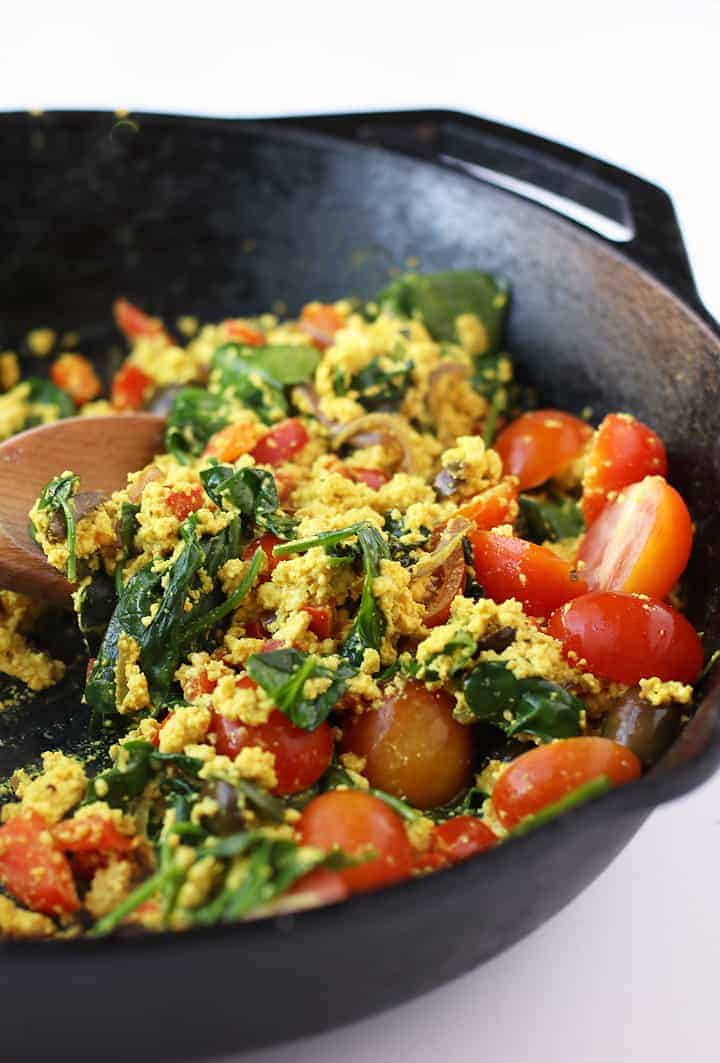 Tofu scramble in a cast iron skillet with a wooden mixing spoon