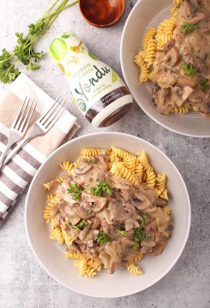 overhead shot of two pasta bowls of vegan mushroom stroganoff on a grey table with a bottle of yondu vegetable umami