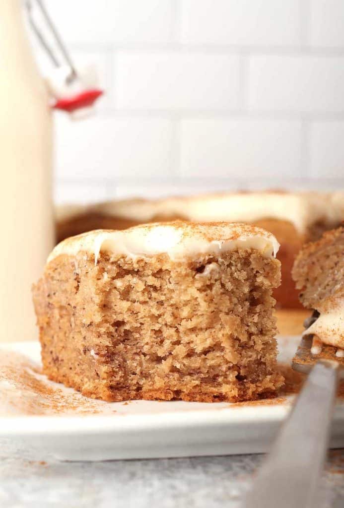 slice of vegan banana cake with cream cheese frosting that has been dusted with cinnamon