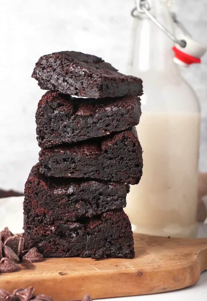 Stack of vegan brownies on a wooden platter with a glass of milk behind. 