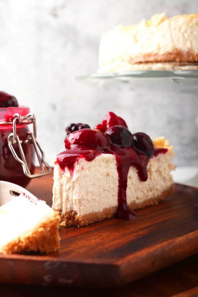 slice of New York style vegan cheesecake on a dark wooden cutting board topped with berry compote