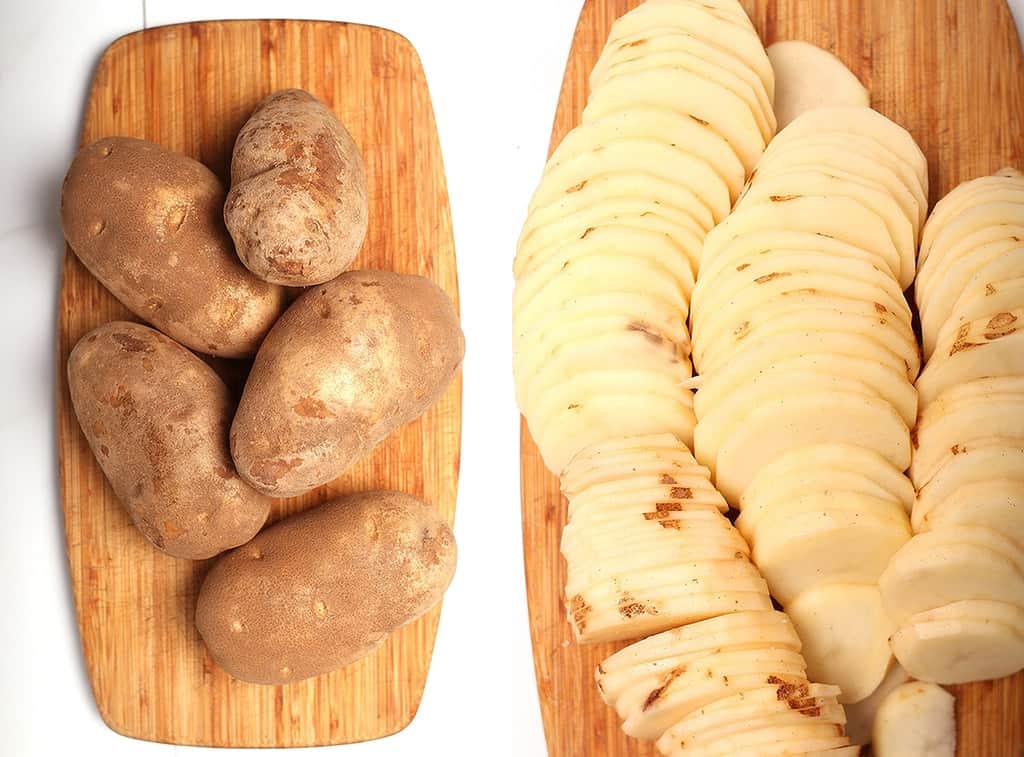 Thinly sliced russet potatoes on a wooden cutting board