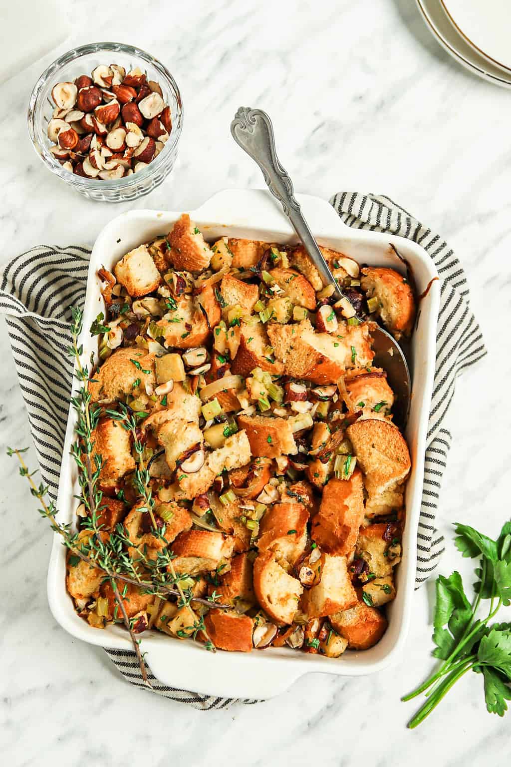Finished vegan stuffing in a casserole dish with a spoon and fresh thyme. 