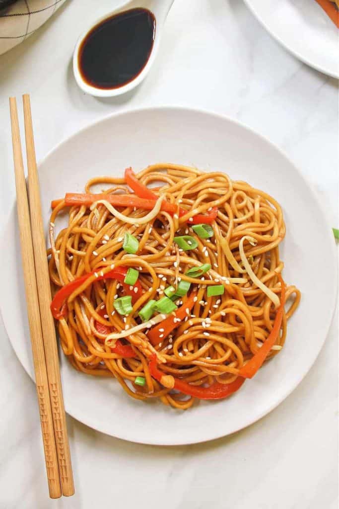 vegan vegetable lo mein on a white plate with chopsticks